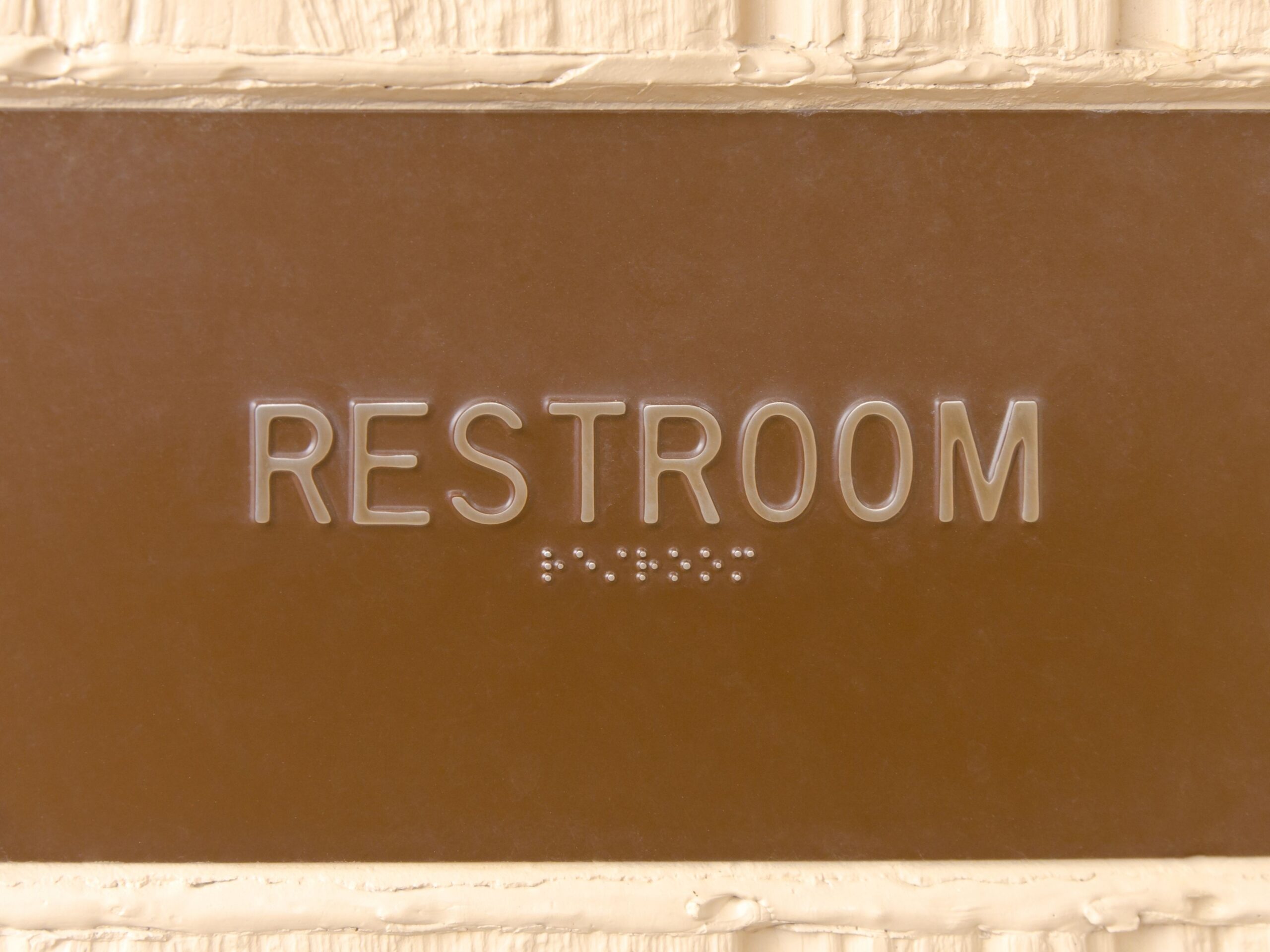 A professional brown restroom sign with white lettering and braille, typical of a modern equestrian center or public facility.