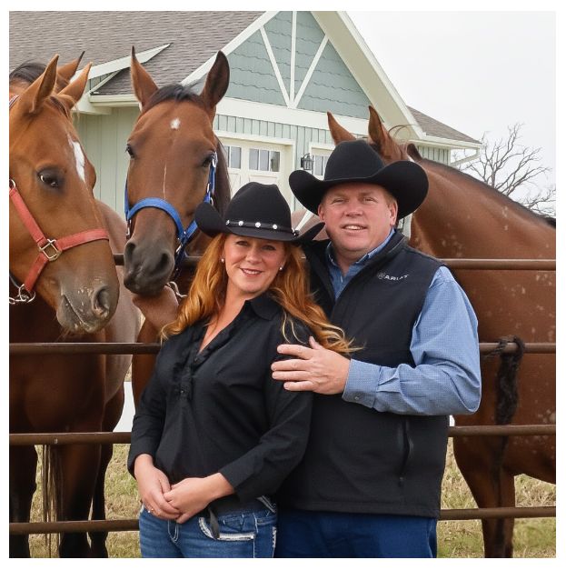 A couple wearing cowboy hats standing by a fence with several horses behind them.